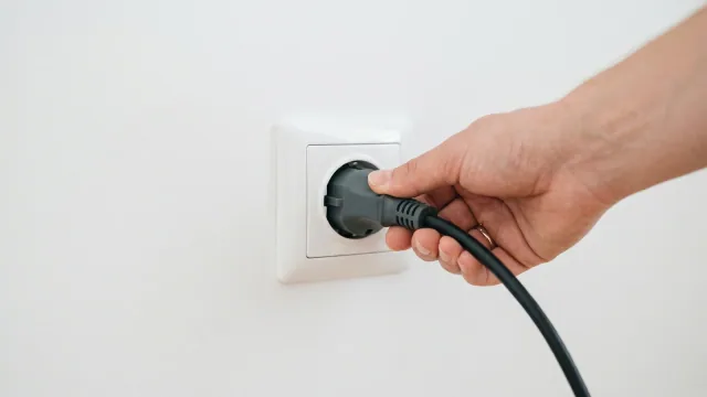 Eine Hand steckt einen grauen Schuko-Stecker mit schwarzem Solarkabel in eine weiße Wandsteckdose — Sinnbild für den jetzt normkonformen Schuko-Anschluss.